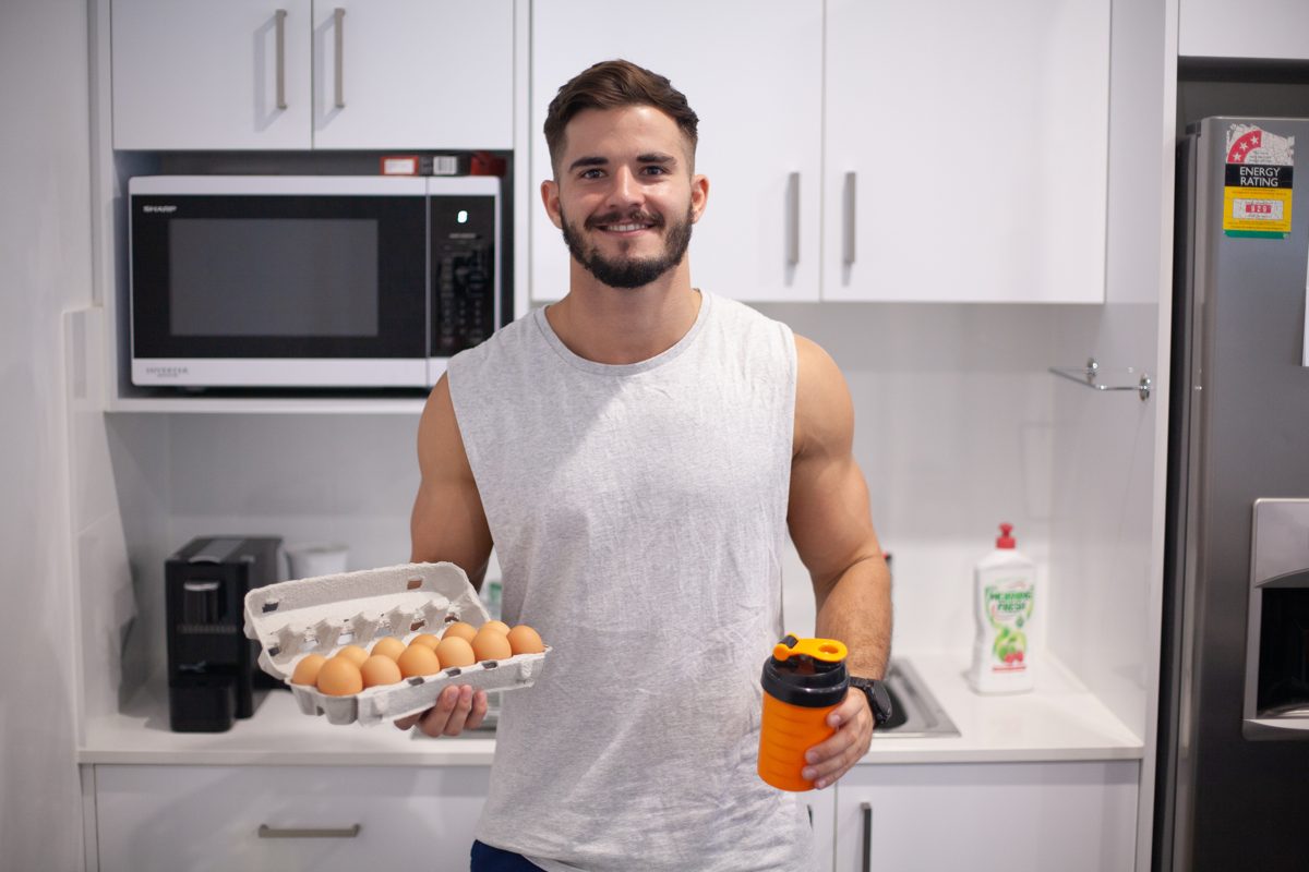 Calum in the kitchen holding eggs and a protein shaker